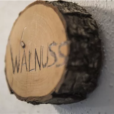 Ein hölzernes Schild mit der Aufschrift „WALNUSS“. Es hängt an einer Wand und hat eine rustikale Ausstrahlung.