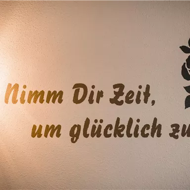 A wall with a quote in German and a stylized rose. It serves as a reminder to take time for happiness.