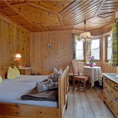 Ein gemütliches Holzzimmer mit zwei Betten und gelben Kissen. Ein Tisch mit Stühlen und einer blühenden Vase vervollständigt die warme Atmosphäre.