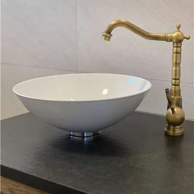 A modern sink made of white ceramic with a golden faucet. The decor is simple and elegant.