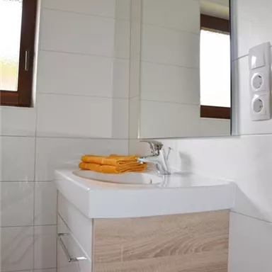 Ein modernes Badezimmer mit einer minimalistisch gestalteten Waschtischanlage. Es gibt helle Fliesen und große Fenster, die für viel Licht sorgen.