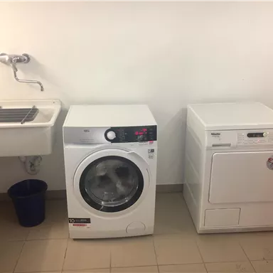 A laundry room with a modern washing machine and a dryer. Next to the appliances is a sink and a blue bucket.