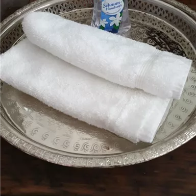 Ein silbernes Tablett mit zwei weißen Handtüchern und einer Flasche Palmolive-Handseife. Die Präsentation ist einfach und stilvoll.