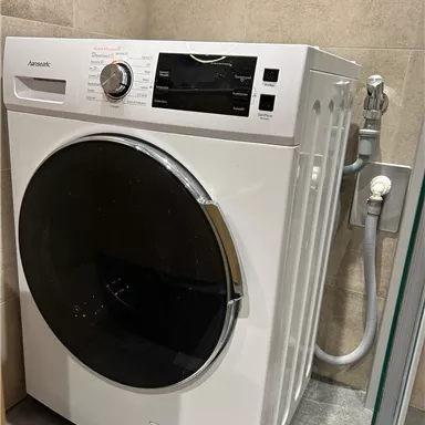 Eine moderne Waschmaschine in einem eleganten Badezimmer. Sie steht an einer Wand und hat ein großes Bullauge sowie verschiedene Bedienelemente.