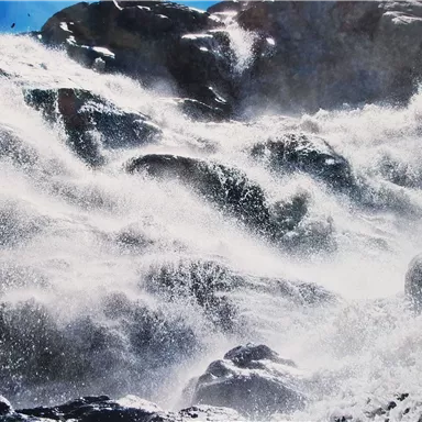 Strong crashing waves hitting large rocks. Splashing water and a dramatic sky in the background.