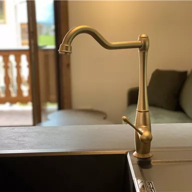 An elegant brass faucet stands above a modern sink. In the background, a cozy living area with a sofa is visible.