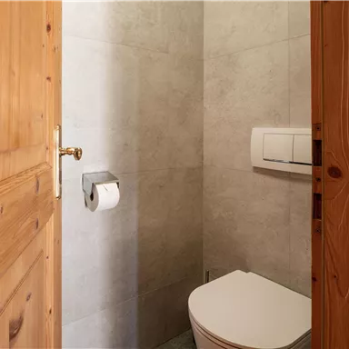 A modern toilet with gray tiles and a wooden door. It is simply and functionally equipped.