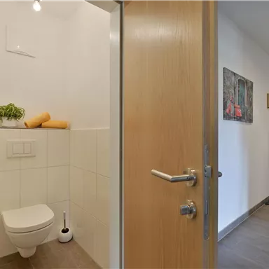 Ein modernes Gäste-WC mit hellen Fliesen und minimalistischem Design. An der Wand hängen dekorative Bilder, und das Umfeld ist gut beleuchtet.