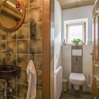 Ein kleines Badezimmer mit Holzdetails und Fliesen. Es gibt ein Waschbecken mit Spiegel und eine Toilette neben einem Fenster.