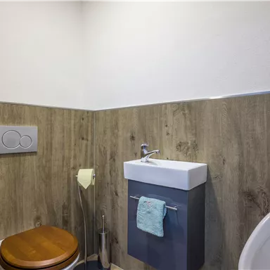 A modern bathroom with wooden paneling. It includes a toilet, a sink, and a towel rack.