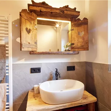 Ein modernes Badezimmer mit einem eleganten Waschbecken auf einem Holztisch. Der Holzspiegel mit Herzen verleiht dem Raum eine gemütliche Atmosphäre.