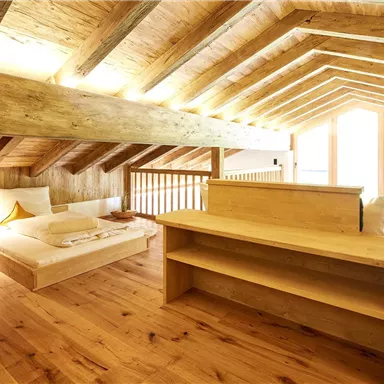 Ein gemütliches Dachzimmer mit Holzdecke und Holzmöbeln. Das Zimmer ist hell und einladend, mit viel natürlichem Licht.