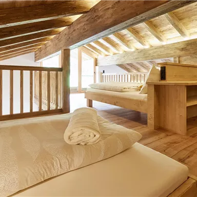 Ein gemütliches Schlafzimmer im Loft-Stil mit Holzdecke und Holzmöbeln. Es gibt zwei Betten, die mit weichen Bettwaren ausgestattet sind.