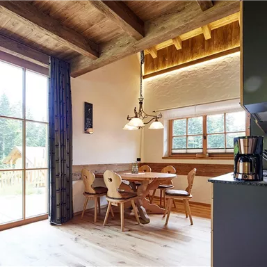 Eine helle und einladende Küche mit einem Essbereich aus Holz. Große Fenster bieten einen Blick ins Grüne.