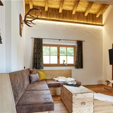 Ein gemütliches Wohnzimmer mit Holzdekor und einer großen Fensterfront. Im Raum befinden sich eine Couch und ein Fernseher, die eine einladende Atmosphäre schaffen.