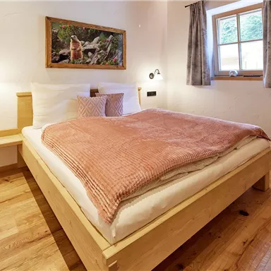 Ein gemütliches Schlafzimmer mit einem großen Bett und warmen Holztönen. Ein Fenster lässt natürliches Licht herein und ein Bild an der Wand sorgt für eine einladende Atmosphäre.