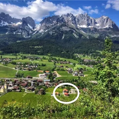 Eine malerische Landschaft mit Bergen im Hintergrund und einem kleinen Dorf im Vordergrund. Die Natur ist grün und üppig, ideal für Erholung und Wandern.