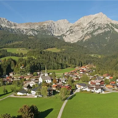 A picturesque mountain landscape with a small village in a green valley. The mountains in the background are majestic and clear.