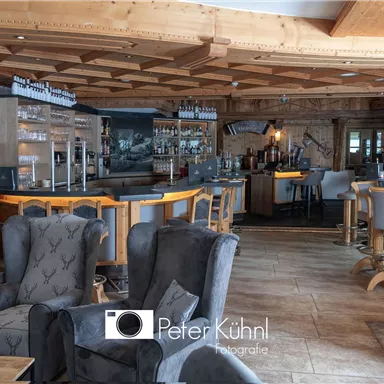 Eine gemütliche Bar mit modernen Möbeln und warmem Holzdekor. Der Raum hat eine einladende Atmosphäre mit einer großen Theke und bequemen Sesseln.