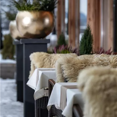 Ein gemütlicher Außenbereich eines Restaurants mit Tischen und Stühlen. Die Umgebung ist winterlich und es liegt Schnee.