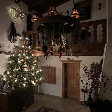 A cozy room with a festively decorated Christmas tree and warm light. The walls are adorned with Christmas decorations and wooden details.