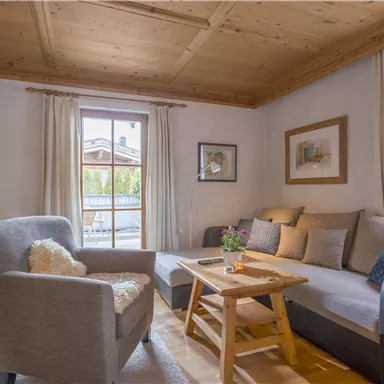 A cozy living room with a gray sofa and a wooden coffee table. Daylight streams through the window, and there is a rustic furniture decor.