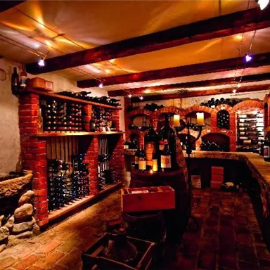 Ein gemütlicher Weinkeller mit Regalen voller Weinflaschen und warmem Licht. Die Wände aus Ziegelsteinen und die rustikale Einrichtung schaffen eine einladende Atmosphäre.