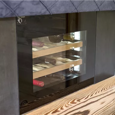 Ein modernes Weinregal mit einem Glasausschnitt. Es zeigt verschiedene Weine auf Holzregalen.