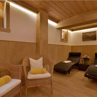 Ein entspannender Wellnessraum mit gemütlichen Liegen und einem warmen Holzdesign. Natürliches Licht strömt durch die Fenster und schafft eine beruhigende Atmosphäre.