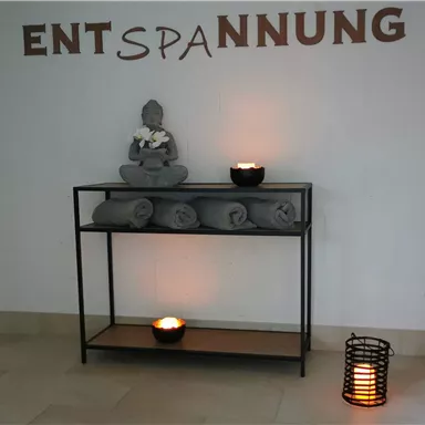 A quiet room with a Buddha statue and folded towels. Soft light from candles creates a relaxing atmosphere.