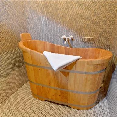 Eine gemütliche Holzbadewanne steht in einem modernen Badezimmer. Die Wände sind mit kleinen Mosaikfliesen gestaltet.