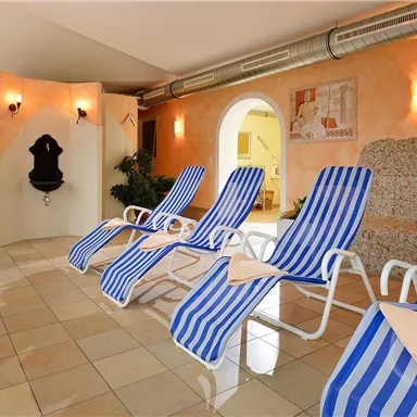 Ein entspannender Wellnessbereich mit Liegen in Blau-weißem Streifenmuster. Pflanzen und sanftes Licht sorgen für eine angenehme Atmosphäre.