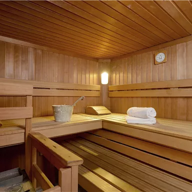 Eine gemütliche Sauna aus Holz mit Bänken und Handtüchern. Ein Eimer und eine Uhr sind ebenfalls im Raum.