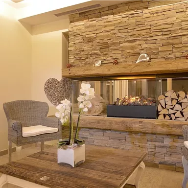 A cozy living space with a modern stone fireplace. Comfortable armchairs and a wooden table create an inviting atmosphere.