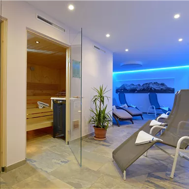 Ein moderner Wellnessbereich mit einer Sauna und Liegen. Die entspannende Atmosphäre wird durch sanfte Beleuchtung und Pflanzen ergänzt.