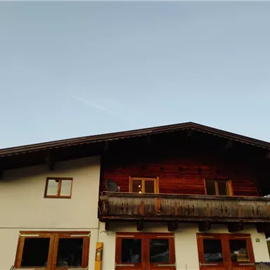 A traditional alpine house with a wooden balcony. The sky is clear and blue.
