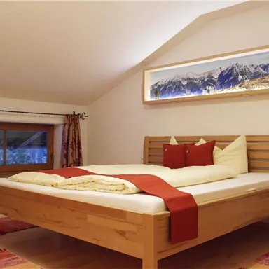 Ein gemütliches Schlafzimmer mit einem großen Bett und Holzergesicht. Die Wände sind hell und es gibt ein Fenster mit Sicht auf die Berge.