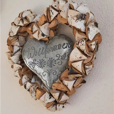 A heart-shaped wreath made of natural materials with a metal sign in the center. The sign reads "Welcome".