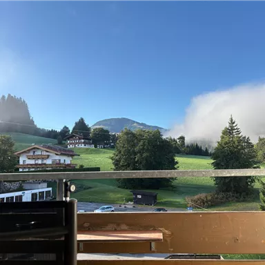 A beautiful view of a mountain landscape with green meadows and trees. In the background, gentle hills and low clouds can be seen.