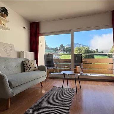 Beautiful living room with a gray sofa and large windows that offer a view of the mountains. The room has bright walls and stylish decoration.