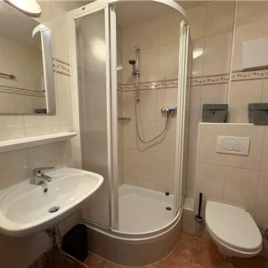 A modern bathroom with a shower, sink, and toilet. The walls are tiled in a light color and the room design is functional.