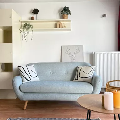A modern living room with a blue sofa and decorative cushions. A round table with candles and a light wall design creates an inviting atmosphere.
