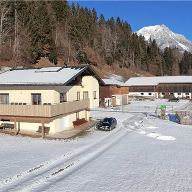 A modern house in a snowy landscape. In the background, mountains and trees can be seen.