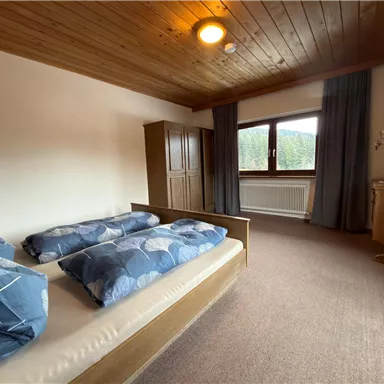 Ein gemütliches Schlafzimmer mit zwei Betten und blauen Bettdecken. Ein Fenster bietet Blick auf die Natur, und der Raum hat Holzdecken und praktische Möbel.