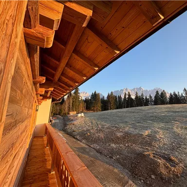 Eine Holzveranda mit Blick auf eine malerische Berglandschaft. Im Hintergrund sind schneebedeckte Gipfel und dichte Wälder zu sehen.