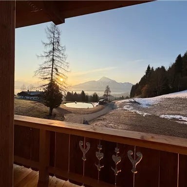 Ein schöner Ausblick vom Balkon mit einem Sonnenuntergang über den Bergen. Die Landschaft ist von Schnee und Bäumen umgeben.