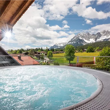 A hot tub on a balcony overlooking the mountains and a picturesque landscape. The clouds break through the sun, creating an inviting atmosphere.
