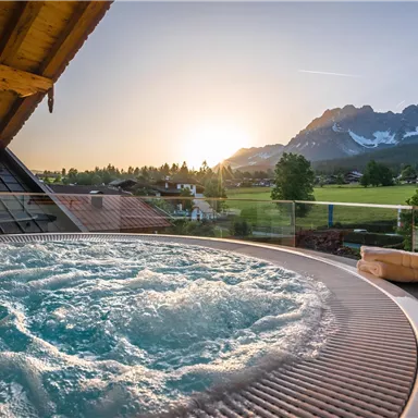 A hot tub with bubbling water on a terrace. In the background, mountains and a beautiful sunset can be seen.