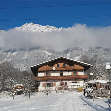 A picturesque chalet in the snowy landscape, surrounded by mountains. The sky is blue and sunny, creating a winter idyll.