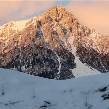 A majestic mountain with a snow-capped peak and gentle slopes. The sky displays soft shades at sunset.